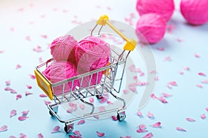 Shopping cart full of wool knitting balls. Knitting background. Pink wool yarns. Colorful pink threads on blue paper background.