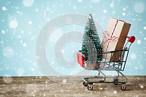 Shopping cart with gift or present and fir tree on snowy effect background. Christmas and New year sale concept. Greeting card. photo