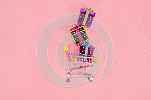 Shopping cart with gifts on pink background with glitter