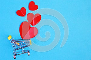 Shopping cart with heart on blue background. Shopper accessory, consumerism and commerce symbol