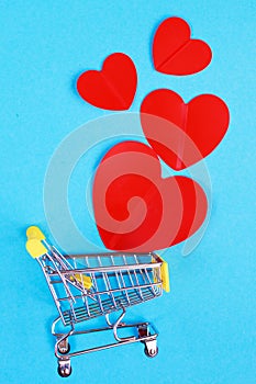 Shopping cart with heart on blue background. Shopper accessory, consumerism and commerce symbol