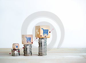 Shopping cart icon and percentage symbol on wood cube blocks on coin stacks as growth graph steps.