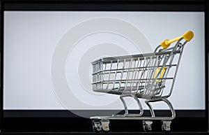 Shopping cart on laptop keyboard. White monitor screen with space for text. Concept of online shopping and online stores