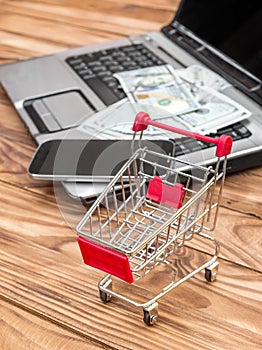 Shopping cart and laptop with money and smartphone on the table. Online shopping and Ecommerce