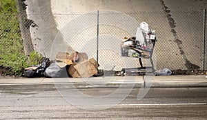 A shopping cart loaded with junk at a homeless camp with wet cardboard boxes