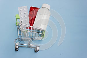 Shopping cart loaded with pills on blue background. The concept of medicine and the sale and delivery of drugs. Copy space