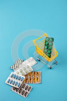 Shopping cart loaded with pills on blue background. The concept of medicine and the sale of drugs. Copy space.