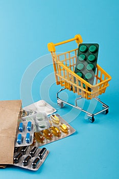 Shopping cart loaded with pills on blue background. The concept of medicine and the sale of drugs. Copy space.