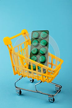 Shopping cart loaded with pills drugs or medicine on yellow background.antibiotics. Women's health, medicine and