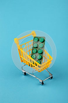 Shopping cart loaded with pills drugs or medicine on yellow background.antibiotics. Women's health, medicine and