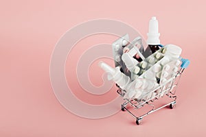 Shopping cart loaded with pills on a pink background. The concept of medicine and the sale of drugs. Copy space