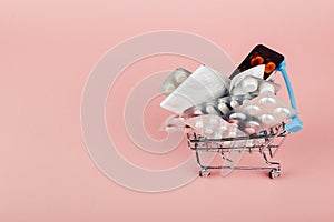 Shopping cart loaded with pills on a pink background. The concept of medicine and the sale of drugs. Copy space