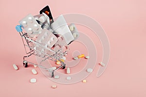 Shopping cart loaded with pills on a pink background. The concept of medicine and the sale of drugs. Copy space