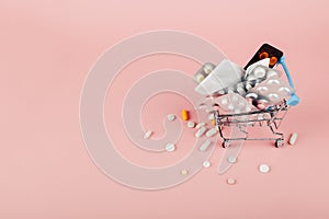 Shopping cart loaded with pills on a pink background. The concept of medicine and the sale of drugs. Copy space