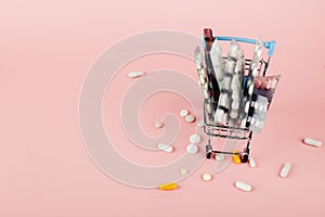Shopping cart loaded with pills on a pink background. The concept of medicine and the sale of drugs. Copy space