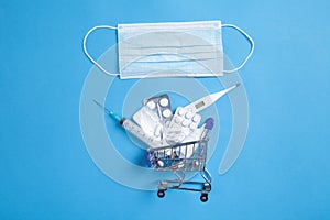 Shopping cart, medical mask, syringe, pills, thermometer on the blue background