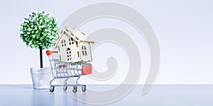 Shopping cart with model of house near gray background with copy space.