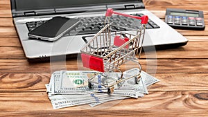 Shopping cart with money and credit card, laptop and smartphone on the table. Online shopping and Ecommerce