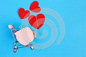 Shopping cart with note paper and hearts on blue background. Shopper accessory, consumerism and commerce symbol