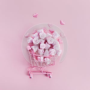 Shopping cart with pink roses and hearts on pink background. Romanitc concept