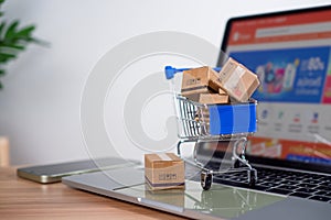 Shopping cart and product boxes placed on laptop computer represent online shopping concept, website, e-commerce, marketplace