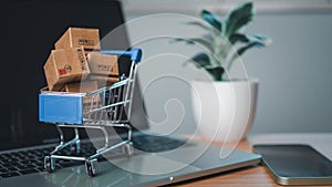 Shopping cart and product boxes placed on laptop computer represent online shopping concept, website, e-commerce, marketplace