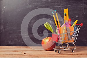 Shopping cart with school supplies over chalkboard background