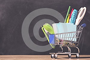 Shopping cart with school supplies over chalkboard background. Back to school sale concept