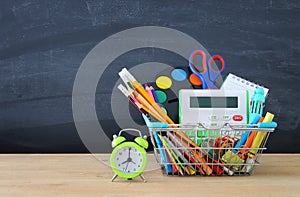 Shopping cart with school supply in front of blackboard. Back to school concept.