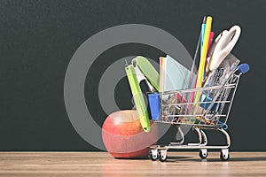 Shopping cart with school supply in front of blackboard. Back to school concept