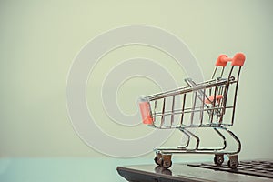 Shopping cart or supermarket trolley with laptop notebook on grey background, e-commerce and online shopping concept.