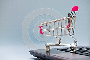 Shopping cart or supermarket trolley with laptop notebook on grey background, e-commerce and online shopping concept.