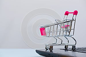 Shopping cart or supermarket trolley with laptop notebook on grey background, e-commerce and online shopping concept