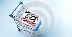 Shopping cart and text ADD VALUE TO YOUR CUSTOMERS on white paper note list. Shopping list concept on blue background