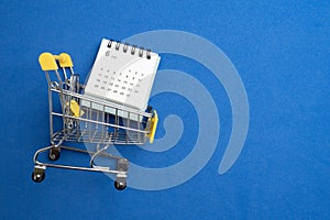 Shopping cart toy and calendar from the supermarket on table with blue background, Sale buy mall market shop consumer concept