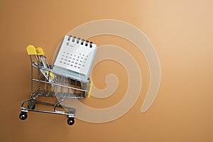 Shopping cart toy and calendar from the supermarket on table with yellow background, Sale buy mall market shop consumer concept.