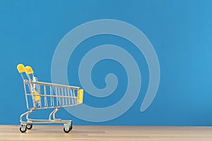 Shopping cart toy from the supermarket on table with blue background, Sale buy mall market shop consumer concept.