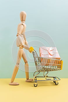 Shopping cart with wooden man mannequin shopping bags. Buying gifts for online shopping, supermarket concept. Vertical