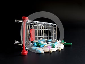 Shopping carts overthrow colorful medicine on black background.