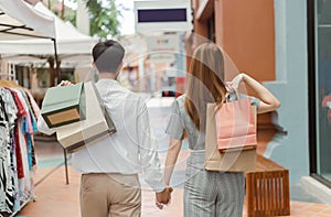 Shopping concept Both male and female shoppers holding each otherâ€™s hand and carrying shopping bags on each back while walking
