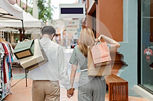 Shopping concept Both male and female shoppers holding each otherâ€™s hand and carrying shopping bags on each back while walking