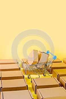 Shopping concept: boxes in blue cart on yellow background. Online shopping consumers can make purchases from home and delivery