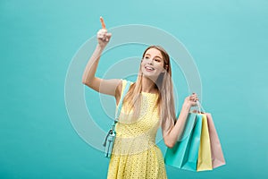 Shopping Concept: Portrait of an excited beautiful girl wearing yellow dress holding shopping bags isolated over blue