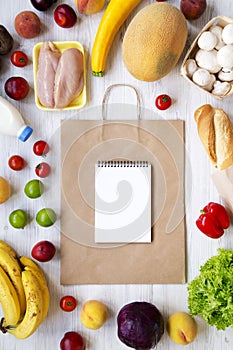 Shopping concept. Set of various groceries with paper bag and blank notepad on white wooden table, top view. Cooking food backgrou