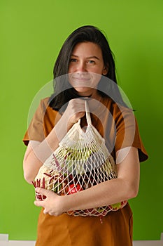 Shopping, consumerism and people concept - smiling young woman with food in bag on green background