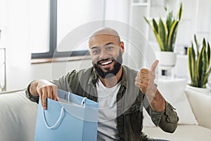 Shopping and delivery concept. Excited latin man opening shopper bag delivered from clothing shop and gesturing thumb up