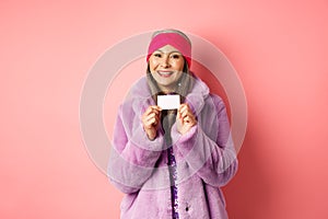 Shopping and fashion concept. Beautiful asian middle-aged woman showing plastic credit card and smiling happy in stylish