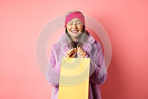 Shopping and fashion concept. Happy asian senior woman in stylish clothes looking happy and delighted, standing with