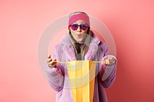 Shopping and fashion concept. Stylish asian elderly woman in sunglasses and faux fur coat open paper bag with gifts