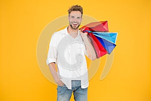 Shopping makes him feel better. Handsome man smiling with shopping bags on yellow background. Happy shopper holding